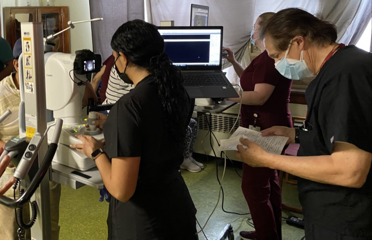 Figure 1. SSSP Volunteers using non-mydriatic retinal cameras to capture images of a patient’s anterior segment and posterior pole (retina), while certified reader Dr. Bernard Szirth interprets patient data. Note subjects as well as imagers all stand at the instruments to streamline the process. When subjects sit at an instrument, the process can take 40% longer. Especially in times of COVID-19, it is important to minimize time at each data collecting station to limit exposure.